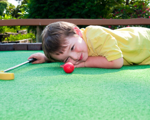 Young boy plays mini golf on putt putt course